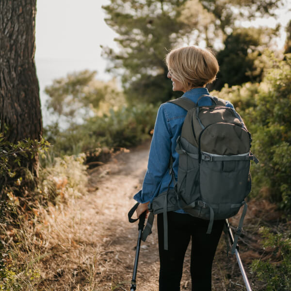 Woman with backpack and walking poles hiking on a trail.